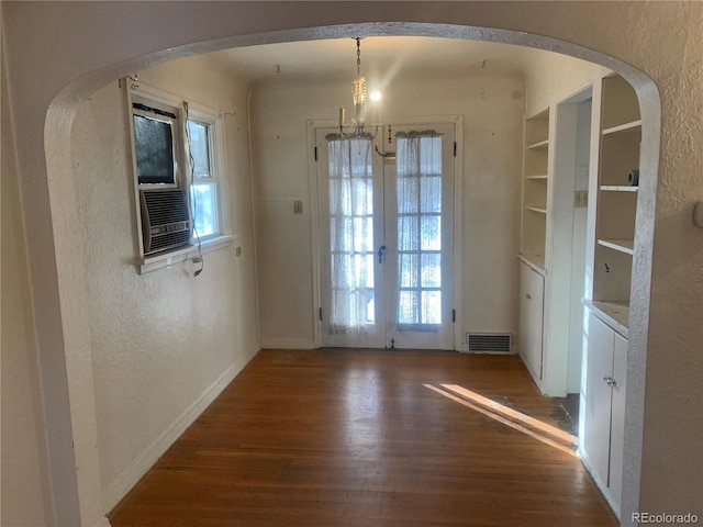 unfurnished dining area with dark wood-type flooring, cooling unit, built in shelves, french doors, and a chandelier