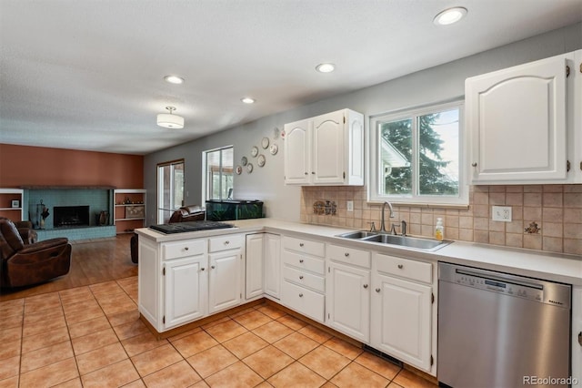 kitchen featuring stainless steel dishwasher, open floor plan, white cabinets, a sink, and a peninsula