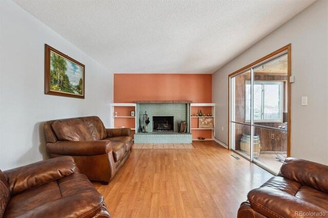 living area featuring a textured ceiling, light wood-type flooring, a fireplace, and visible vents