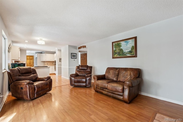 living room with baseboards, light wood-style flooring, and a textured ceiling