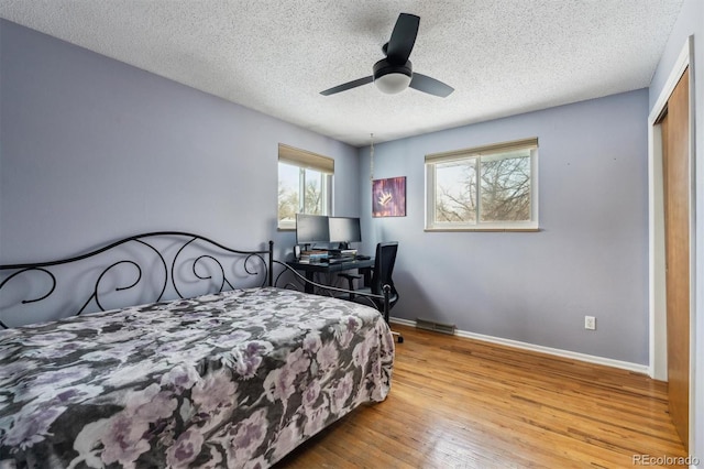 bedroom featuring a textured ceiling, ceiling fan, light wood-style flooring, visible vents, and baseboards