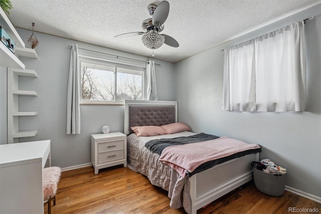 bedroom with light wood-type flooring, ceiling fan, a textured ceiling, and baseboards