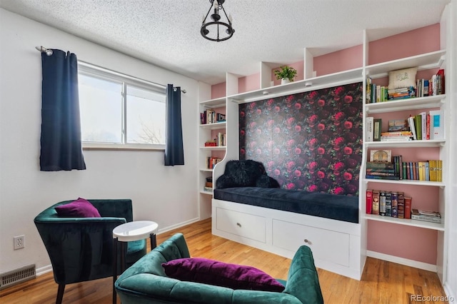 living area featuring visible vents, a textured ceiling, baseboards, and wood finished floors