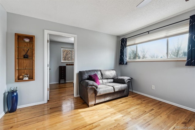 living area with light wood-type flooring, baseboards, and a textured ceiling