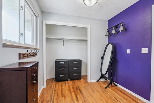 bedroom with a textured ceiling, a closet, light wood-style flooring, and baseboards