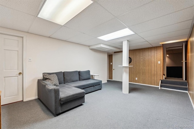 living area with wood walls, carpet, baseboards, and a drop ceiling