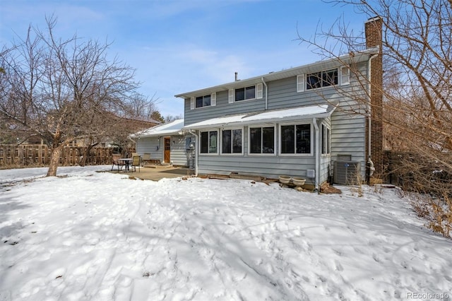 snow covered rear of property featuring fence and a chimney