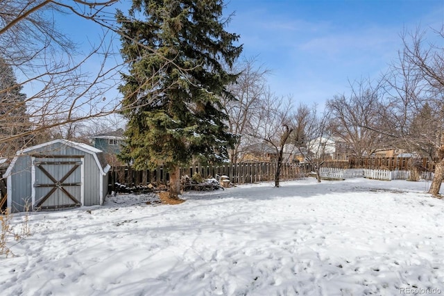 yard covered in snow featuring an outbuilding, a fenced backyard, and a storage shed