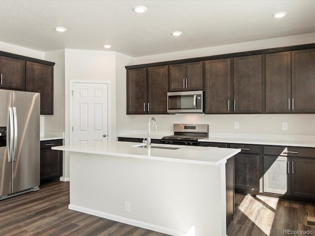 kitchen featuring a kitchen island with sink, stainless steel appliances, a sink, dark brown cabinets, and light countertops