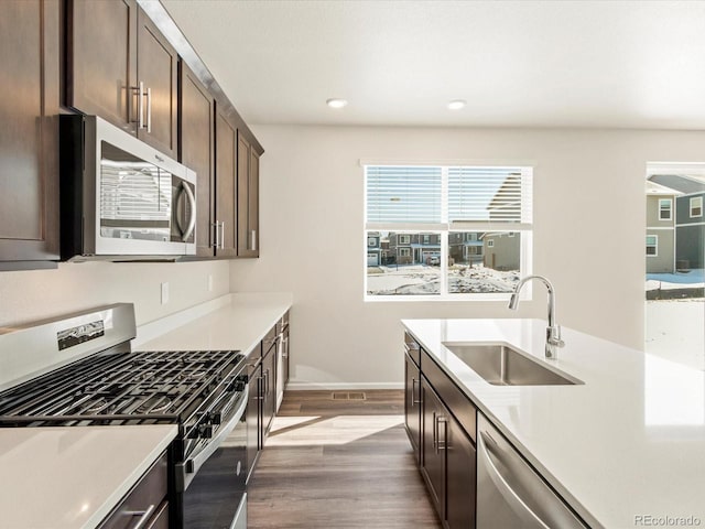 kitchen featuring dark brown cabinets, appliances with stainless steel finishes, light countertops, and a sink