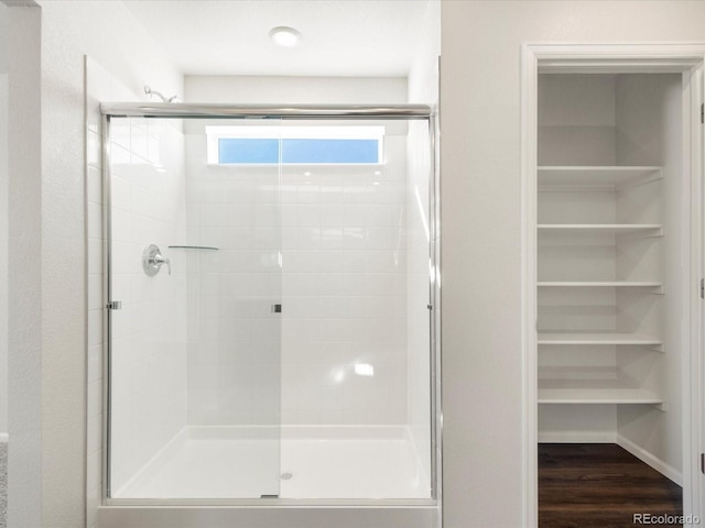 bathroom with a shower stall, a spacious closet, and wood finished floors