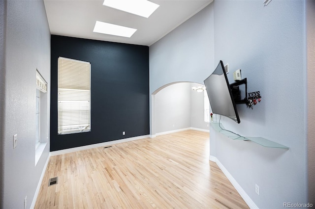 spare room featuring baseboards, vaulted ceiling with skylight, wood finished floors, and visible vents