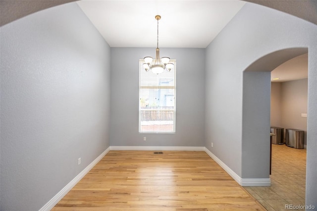 unfurnished room featuring arched walkways, a chandelier, light wood finished floors, and baseboards