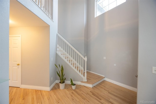 staircase featuring baseboards, a towering ceiling, and wood finished floors