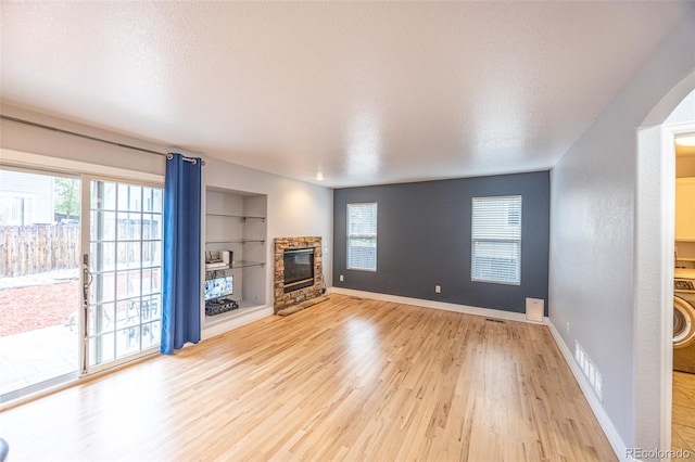 unfurnished living room with a wealth of natural light, a stone fireplace, and light wood-style flooring