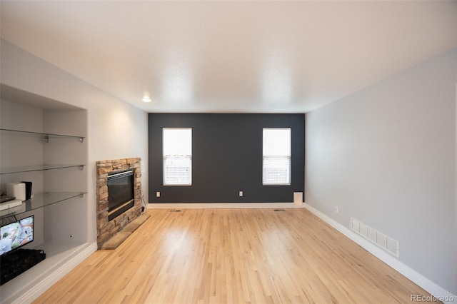 unfurnished living room with light wood-style flooring, visible vents, baseboards, and a stone fireplace