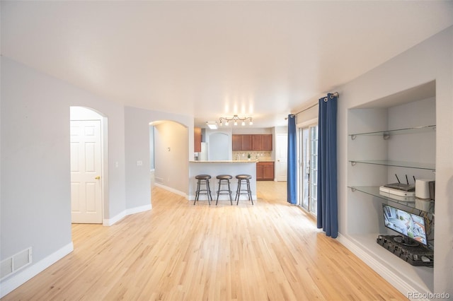 living room with baseboards, arched walkways, visible vents, and light wood-type flooring