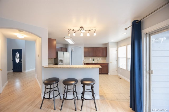 kitchen featuring backsplash, light countertops, arched walkways, a peninsula, and refrigerator with ice dispenser