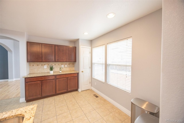 kitchen with visible vents, light tile patterned floors, arched walkways, baseboards, and decorative backsplash