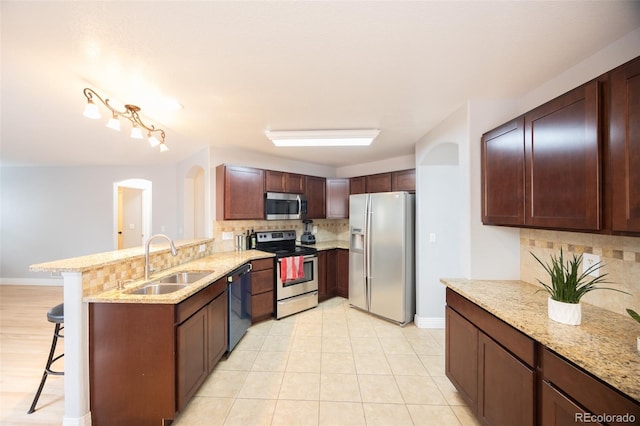 kitchen featuring stainless steel appliances, a sink, a peninsula, tasteful backsplash, and a breakfast bar area