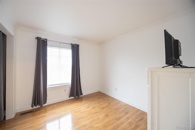 spare room with light wood-style flooring, visible vents, baseboards, and ornamental molding