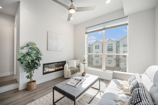 interior space with baseboards, a ceiling fan, a glass covered fireplace, wood finished floors, and recessed lighting