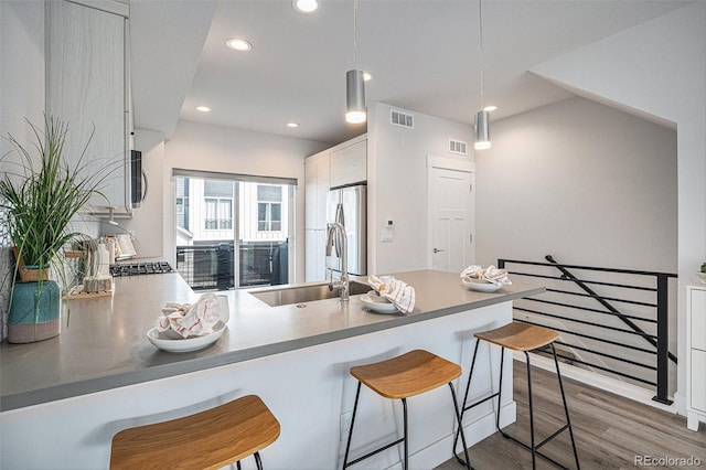 kitchen featuring freestanding refrigerator, wood finished floors, a sink, and visible vents