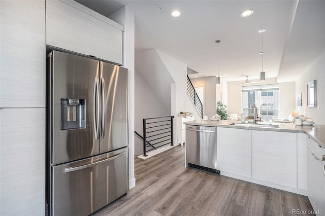 kitchen featuring modern cabinets, appliances with stainless steel finishes, wood finished floors, white cabinetry, and a sink