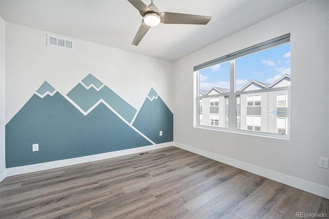 unfurnished room with ceiling fan, wood finished floors, visible vents, and baseboards