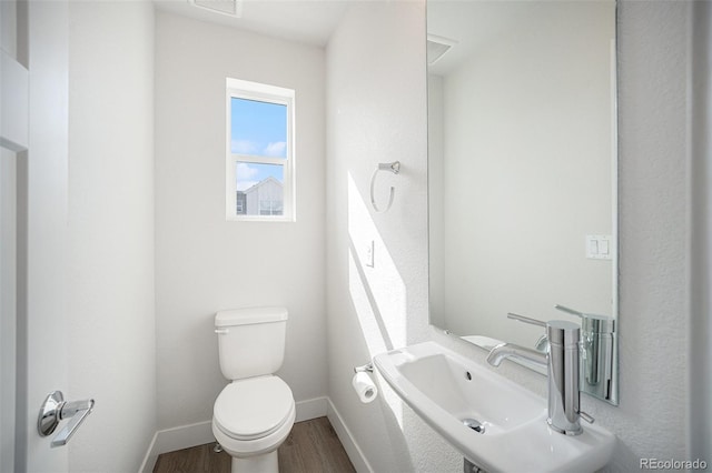 half bathroom featuring visible vents, baseboards, toilet, wood finished floors, and a sink