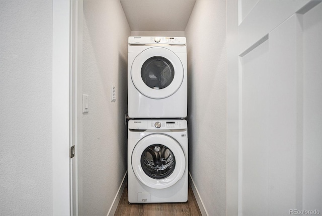 clothes washing area with stacked washer and dryer, laundry area, baseboards, a textured wall, and wood finished floors