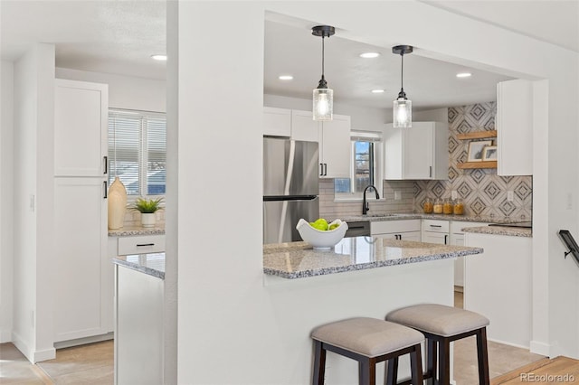 kitchen featuring stainless steel refrigerator, decorative light fixtures, white cabinetry, backsplash, and light stone counters