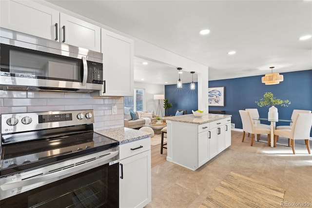 kitchen with appliances with stainless steel finishes, light stone counters, decorative backsplash, white cabinets, and decorative light fixtures