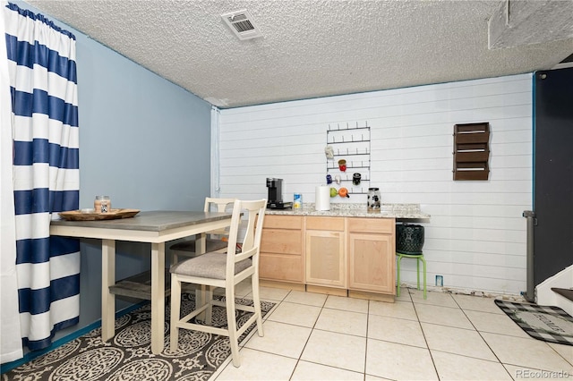 kitchen with light brown cabinets, a textured ceiling, light tile patterned floors, and wooden walls