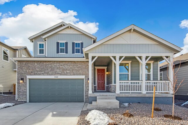 view of front of home with stone siding, covered porch, an attached garage, and driveway