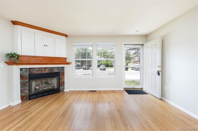 3098 W 107th Pl Unit C, Westminster, CO 80031 - unfurnished living room featuring light wood-type flooring, a glass covered fireplace, a textured ceiling, healthy amount of natural light, and baseboards