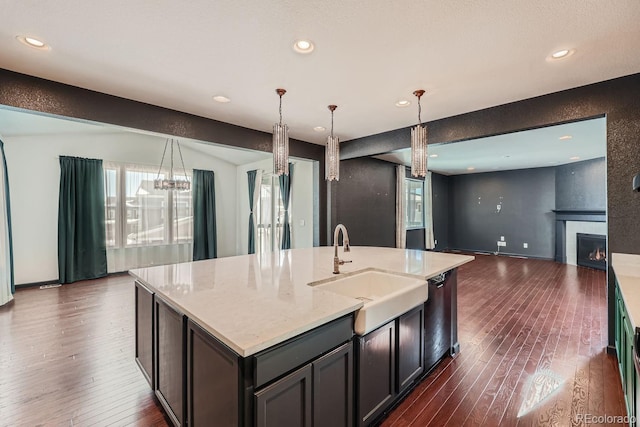 kitchen featuring decorative light fixtures, dishwasher, sink, a large fireplace, and a center island with sink