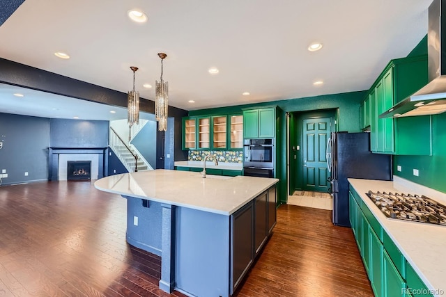 kitchen featuring pendant lighting, wall chimney range hood, a large fireplace, an island with sink, and stainless steel gas cooktop