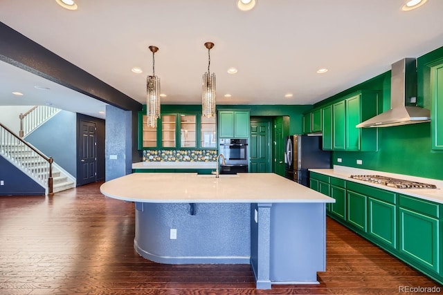 kitchen with black refrigerator, pendant lighting, stainless steel gas stovetop, a center island with sink, and wall chimney range hood