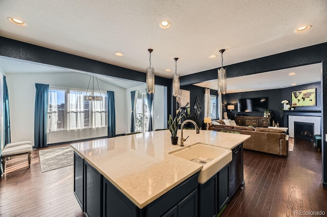 kitchen featuring a kitchen island with sink, decorative light fixtures, a fireplace, and dark hardwood / wood-style floors