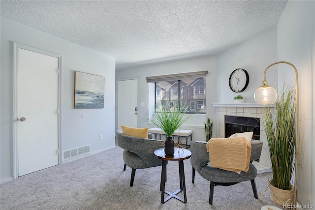 sitting room featuring a textured ceiling, carpet flooring, and a tile fireplace