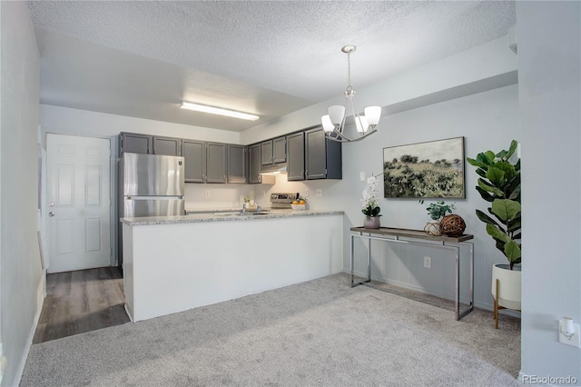 kitchen featuring a textured ceiling, kitchen peninsula, light carpet, appliances with stainless steel finishes, and decorative light fixtures