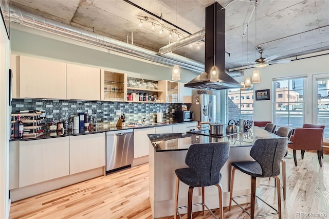 kitchen with ceiling fan, island exhaust hood, backsplash, stainless steel appliances, and light hardwood / wood-style floors