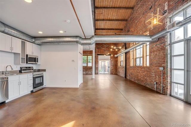 3033 Blake St Unit 121, Denver, CO 80205 - kitchen featuring appliances with stainless steel finishes, brick wall, finished concrete flooring, white cabinetry, and recessed lighting