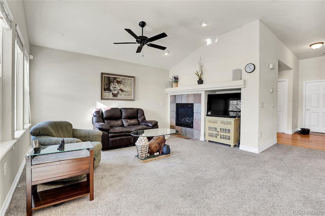 carpeted living room with baseboards, vaulted ceiling, a tiled fireplace, and ceiling fan