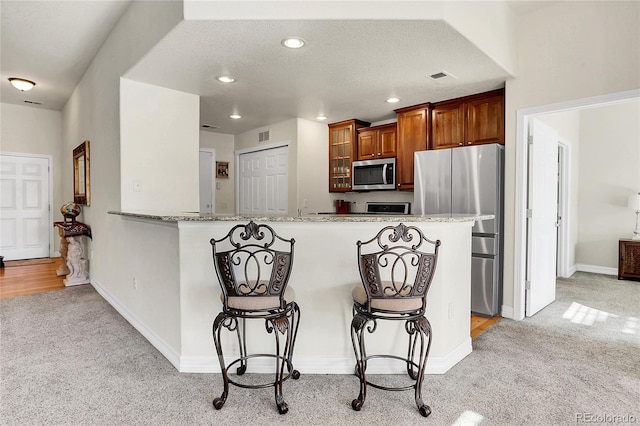 kitchen featuring light carpet, stainless steel appliances, a breakfast bar, and light stone countertops