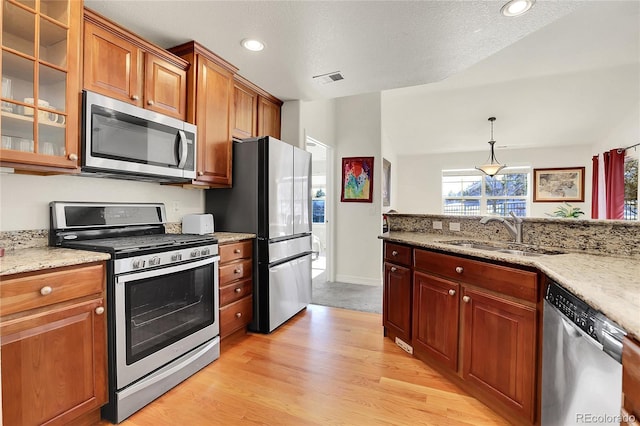 kitchen with brown cabinetry, glass insert cabinets, stainless steel appliances, light wood-type flooring, and a sink