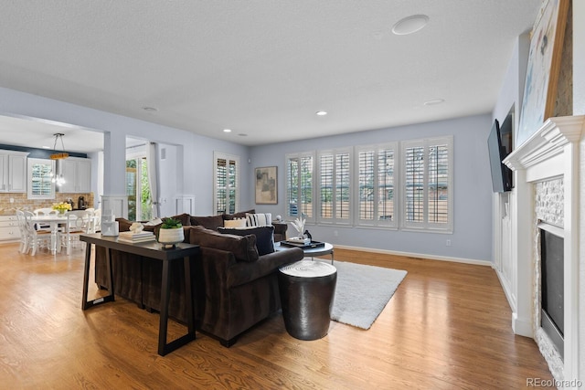 living area with baseboards, a fireplace, recessed lighting, and light wood-style flooring