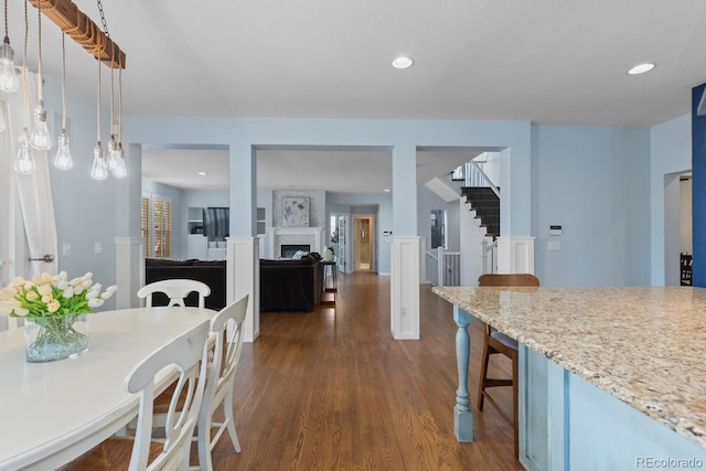 kitchen with light stone counters, dark wood-style floors, a fireplace, a kitchen bar, and pendant lighting