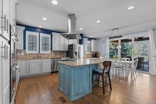 kitchen featuring light stone counters, a kitchen island, island exhaust hood, backsplash, and stainless steel appliances